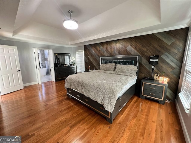 bedroom featuring a raised ceiling, connected bathroom, wood walls, and light hardwood / wood-style flooring