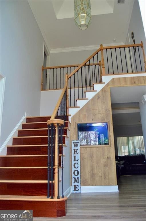 stairs featuring hardwood / wood-style floors, a towering ceiling, and ornamental molding