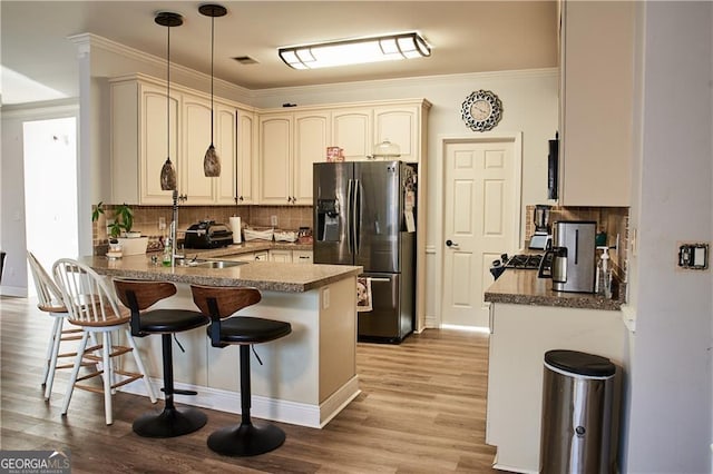 kitchen with kitchen peninsula, sink, pendant lighting, light hardwood / wood-style flooring, and stainless steel fridge with ice dispenser