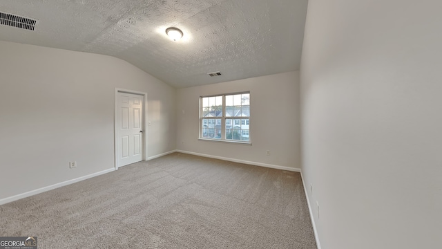 spare room featuring carpet, a textured ceiling, and vaulted ceiling