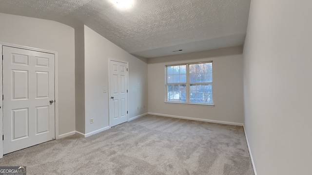 unfurnished bedroom with a textured ceiling, light colored carpet, and vaulted ceiling