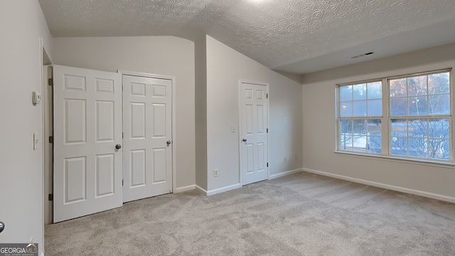 unfurnished bedroom with a textured ceiling, light colored carpet, and lofted ceiling