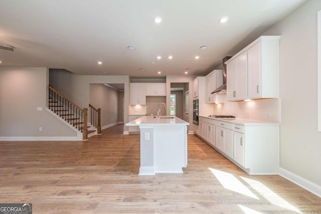 kitchen featuring light wood-type flooring, sink, a center island with sink, white cabinetry, and stainless steel gas stovetop