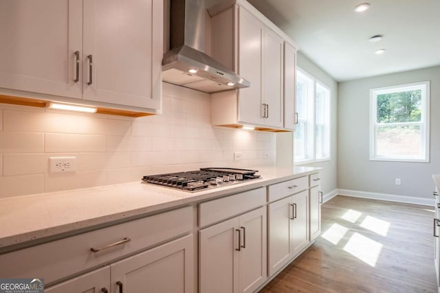 kitchen with white cabinets, stainless steel gas stovetop, light stone counters, and wall chimney range hood