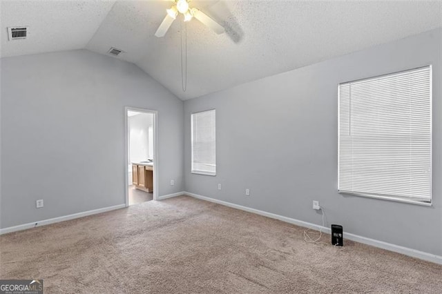 carpeted empty room featuring a textured ceiling, vaulted ceiling, and ceiling fan