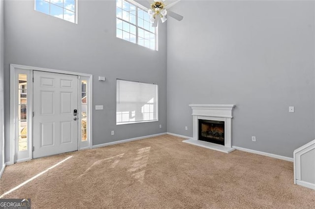 unfurnished living room featuring a wealth of natural light, ceiling fan, a towering ceiling, and light colored carpet