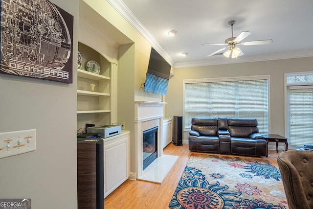 living room with ceiling fan, built in features, ornamental molding, and light wood-type flooring