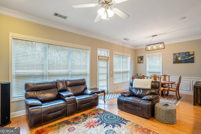 living room with crown molding, light hardwood / wood-style flooring, a healthy amount of sunlight, and ceiling fan with notable chandelier