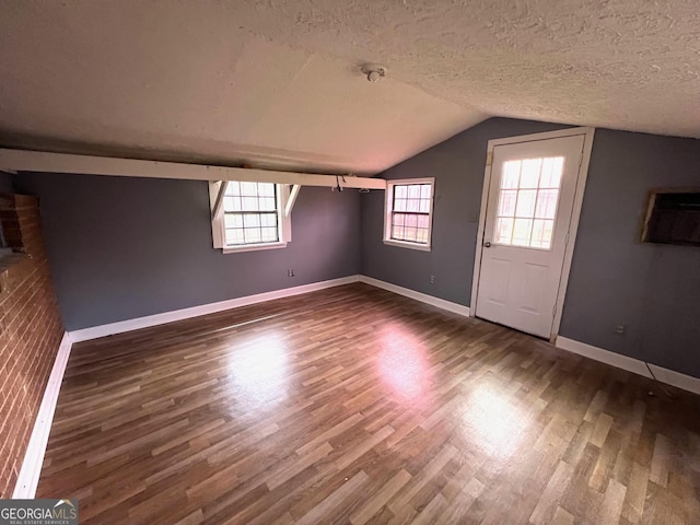 additional living space with dark hardwood / wood-style flooring, a textured ceiling, and vaulted ceiling