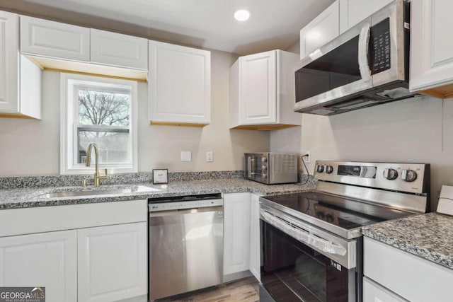 kitchen featuring light stone countertops, white cabinetry, sink, stainless steel appliances, and light hardwood / wood-style floors