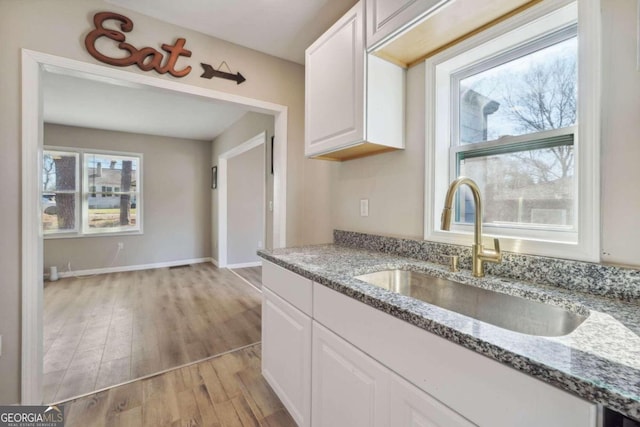 kitchen featuring light stone countertops, sink, white cabinets, and light hardwood / wood-style floors