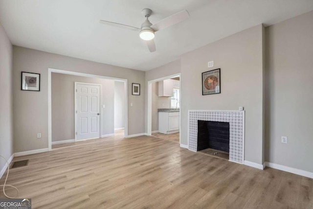 unfurnished living room with a tile fireplace, ceiling fan, and light wood-type flooring