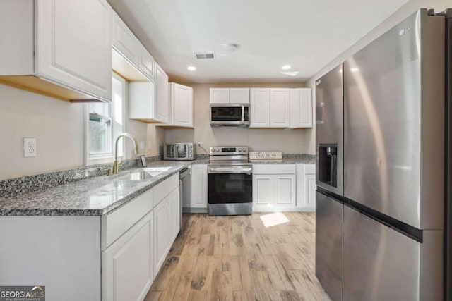 kitchen featuring sink, appliances with stainless steel finishes, light hardwood / wood-style floors, light stone counters, and white cabinetry