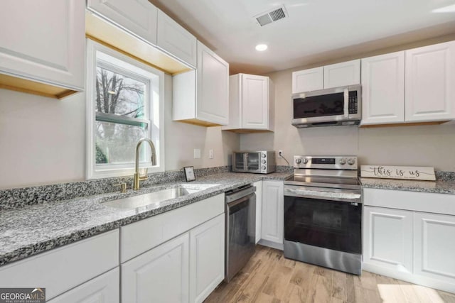 kitchen with light stone countertops, appliances with stainless steel finishes, white cabinetry, and sink