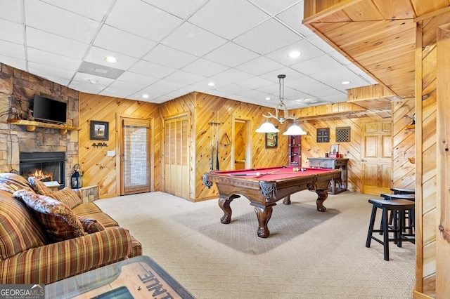 playroom with carpet flooring, a paneled ceiling, pool table, a stone fireplace, and wood walls