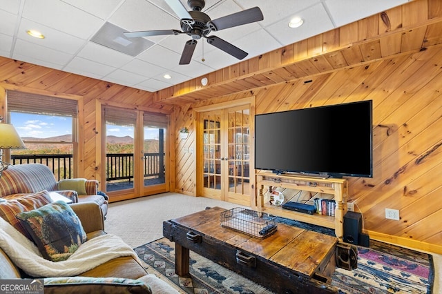 carpeted living room with french doors, ceiling fan, and wood walls