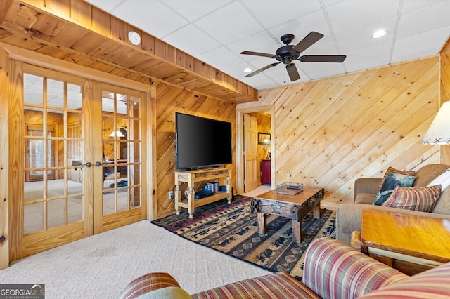 carpeted living room featuring ceiling fan, french doors, and wooden walls