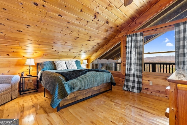 bedroom featuring a mountain view, wood walls, lofted ceiling, light hardwood / wood-style flooring, and wood ceiling