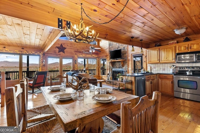 dining space with ceiling fan with notable chandelier, wooden ceiling, a fireplace, and light hardwood / wood-style flooring