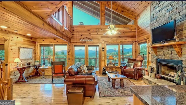 living room featuring high vaulted ceiling, ceiling fan, a fireplace, light hardwood / wood-style floors, and wood ceiling