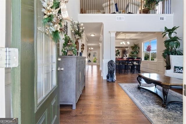 foyer featuring coffered ceiling, ornate columns, wood-type flooring, a notable chandelier, and beam ceiling