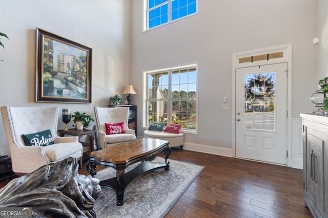 living area with a towering ceiling, a wealth of natural light, and dark hardwood / wood-style flooring