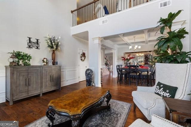 living room featuring dark hardwood / wood-style floors, decorative columns, a chandelier, coffered ceiling, and beam ceiling