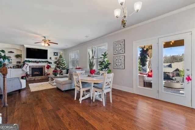 dining space with built in shelves, ornamental molding, dark hardwood / wood-style flooring, a fireplace, and ceiling fan with notable chandelier