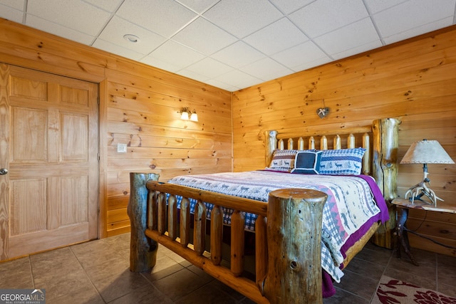 bedroom featuring a paneled ceiling, dark tile patterned flooring, and wood walls