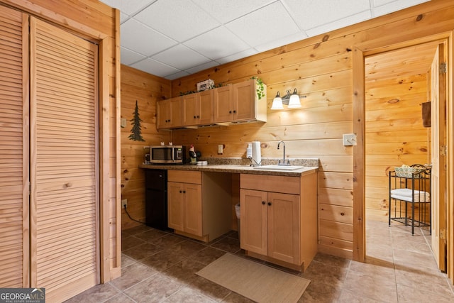 kitchen with light brown cabinetry, wooden walls, a drop ceiling, refrigerator, and sink