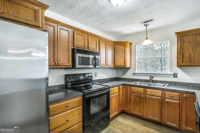 kitchen with sink, light wood-type flooring, a textured ceiling, appliances with stainless steel finishes, and decorative light fixtures