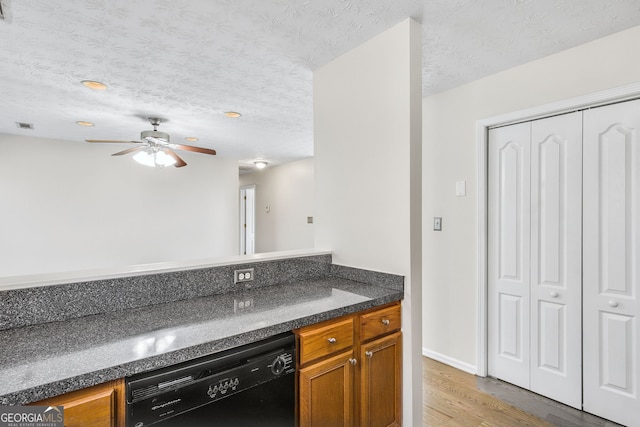 kitchen featuring light wood-type flooring, a textured ceiling, ceiling fan, dark stone countertops, and dishwasher