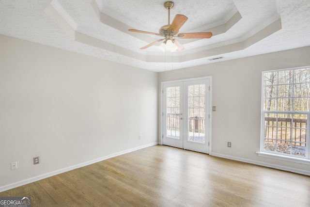 unfurnished room featuring french doors, ceiling fan, a textured ceiling, a tray ceiling, and light hardwood / wood-style floors