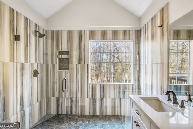 bathroom with tiled shower, vanity, and lofted ceiling