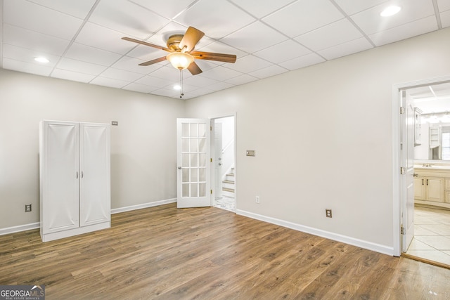 unfurnished bedroom featuring french doors, ensuite bathroom, a drop ceiling, ceiling fan, and wood-type flooring