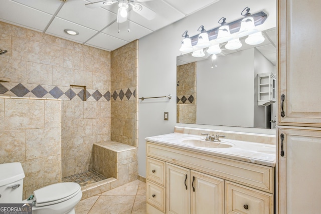 bathroom with vanity, ceiling fan, tiled shower, tile patterned flooring, and toilet