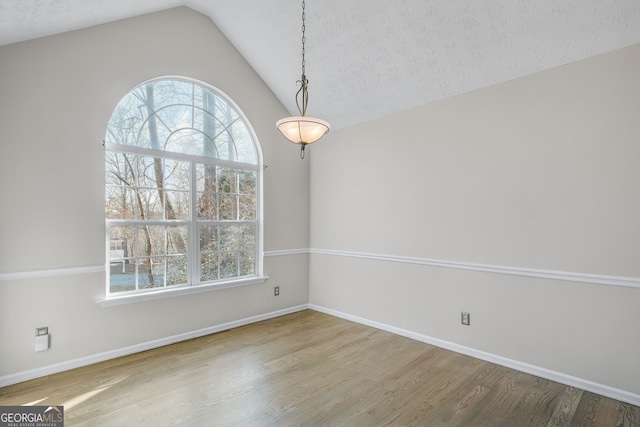 spare room with vaulted ceiling, hardwood / wood-style floors, and a textured ceiling