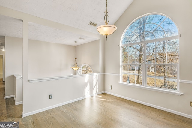 unfurnished dining area featuring hardwood / wood-style floors, a textured ceiling, and lofted ceiling