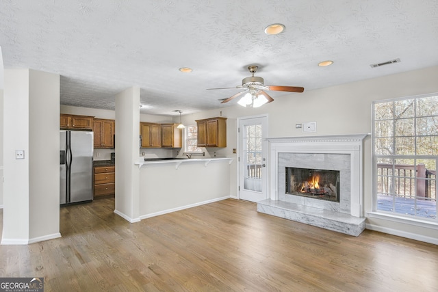 unfurnished living room with ceiling fan, light wood-type flooring, a premium fireplace, and a textured ceiling