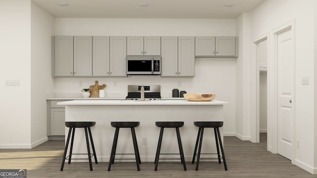 kitchen featuring a center island with sink, gray cabinets, a kitchen bar, and range