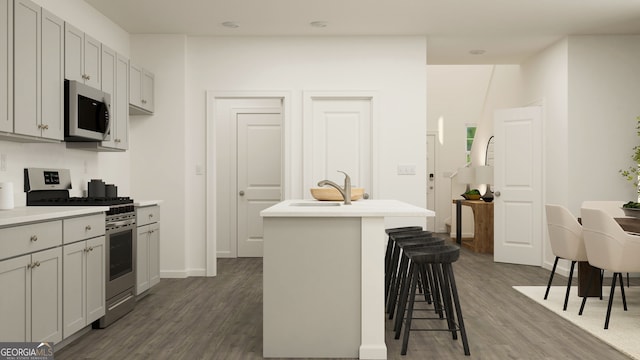 kitchen with a kitchen island with sink, a kitchen breakfast bar, sink, appliances with stainless steel finishes, and dark hardwood / wood-style flooring