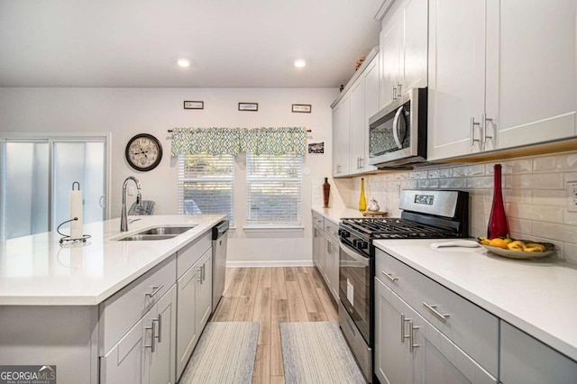 kitchen featuring appliances with stainless steel finishes, backsplash, a kitchen island with sink, light hardwood / wood-style flooring, and sink