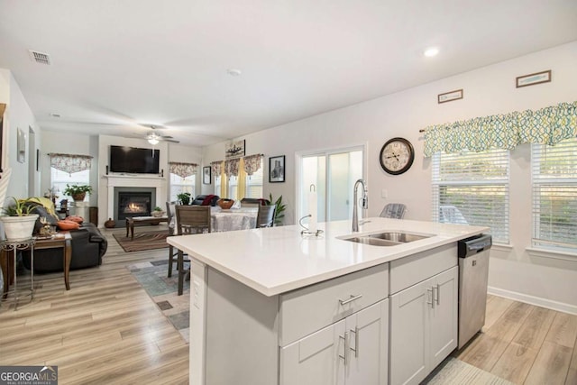 kitchen with light hardwood / wood-style floors, stainless steel dishwasher, a center island with sink, sink, and white cabinetry