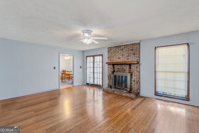 unfurnished living room with a brick fireplace, a textured ceiling, ceiling fan, and light hardwood / wood-style flooring