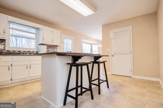 kitchen featuring decorative backsplash, a kitchen breakfast bar, white cabinetry, and a wealth of natural light