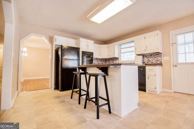 kitchen featuring backsplash, black appliances, white cabinets, a kitchen island, and a breakfast bar area