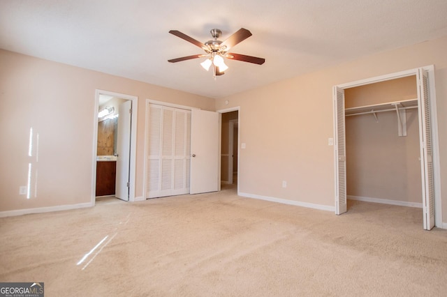 unfurnished bedroom with ceiling fan, light colored carpet, connected bathroom, and two closets