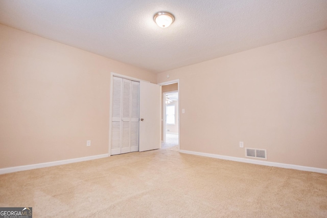 unfurnished bedroom featuring a textured ceiling, light colored carpet, and a closet