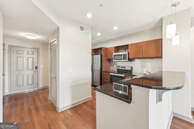 kitchen featuring kitchen peninsula, appliances with stainless steel finishes, decorative light fixtures, dark hardwood / wood-style floors, and a breakfast bar area