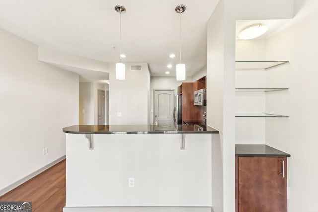 kitchen featuring dark wood-type flooring, stainless steel appliances, a kitchen breakfast bar, kitchen peninsula, and decorative light fixtures